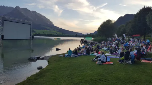 Filmvorführung im Freien, Kinoleinwand im Wasser und Zuseher am Ufer.